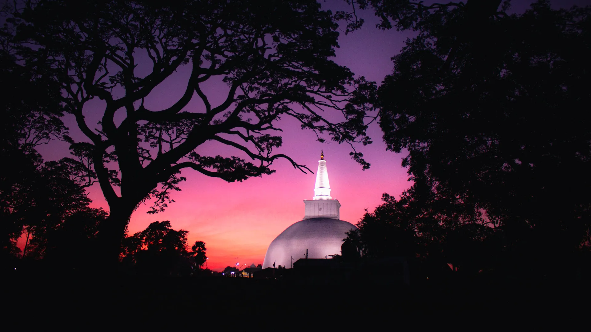Ancient white stupa silhouetted against a vibrant purple and orange sunset.